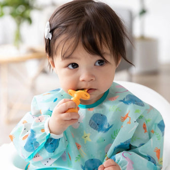 A toddler uses Bumkins Silicone Chewtensils®: Tangerine, a teething toy made of 100% food-safe silicone, while wearing a sea creature bib.