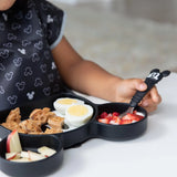 A child holds a Mickey Mouse fork from Bumkins set, enjoying strawberries from a Mickey-shaped plate with waffles, eggs, and apples.