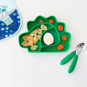 Dinosaur-shaped plate with pasta, carrots, and an egg. Nearby: Bumkins Spoon + Fork: Jade toddler utensils and a bib.