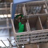 In a dishwasher, place two Bumkins Spoon + Fork: Jade toddler utensils in the cutlery basket.