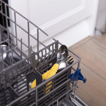 Open dishwasher with gray rack displays Bumkins Spoon + Fork: Pineapple with yellow handles and other silverware; white door in background.