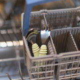 Two baby utensils from Bumkins, the Spoon + Fork: Sage, stand in the cutlery basket of an open dishwasher.