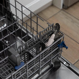 Open dishwasher with the Bumkins Spoon + Fork in Sand, inside a gray utensil holder. Kitchen floor is visible in the background.