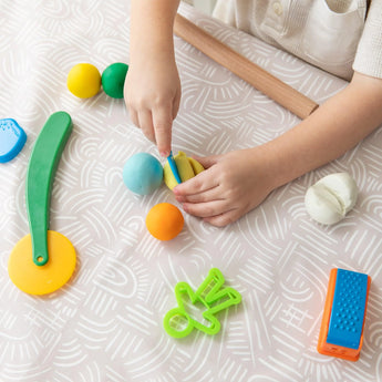 A child plays with colorful playdough on the vibrant, machine washable Splat Mat: Wander by Bumkins, ideal for creative messes.