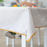 A child plays on the Bumkins Splat Mat: Wander, featuring waterproof fabric with a white pattern and orange trim.