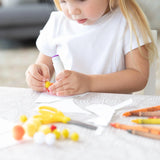 A child crafting with glue, pom-poms, scissors, and crayons on the Bumkins Splat Mat: Wander for easy cleanup.