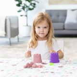 A girl plays with sand molds on the Bumkins Splat Mat: Floral, with a sofa and plant background for easy cleaning.