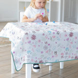 A child crafts on a Bumkins Splat Mat: Floral, wearing a white shirt, ensuring easy cleanup in the cozy home.