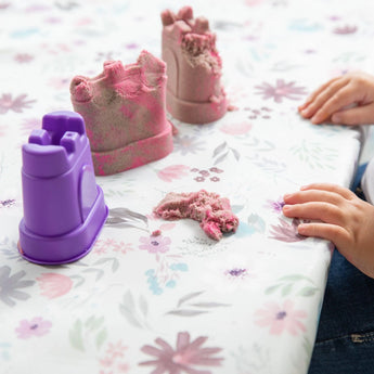 A child plays with purple and pink sandcastle molds on the Bumkins Splat Mat: Floral, ensuring easy cleanup.