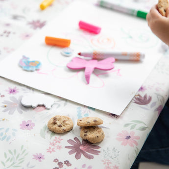 A child draws on the Bumkins Splat Mat: Floral with cookies, markers, and cutouts, making cleanup a breeze.