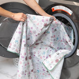 A person places a Splat Mat: Floral by Bumkins into a front-loading washer, enjoying the ease of cleaning.