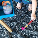 A childs hands and feet on the Bumkins Be Kind Splat Mat adorned with colorful stick-ons, doodles, and a nearby jar of paint.