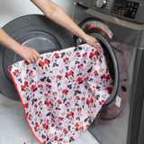 Person loading a pink Splat Mat: Minnie Mouse by Bumkins into a front-loading washer, ideal for easy-wipe or waterproof fabric care.