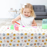 A young girl smiles while painting on a Bumkins Splat Mat: Winnie and Friends, featuring colorful cartoon animal patterns.