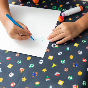 Child draws with a blue marker on paper, surrounded by the colorful Super Mario™ Lineup Splat Mat, waterproof from Bumkins.