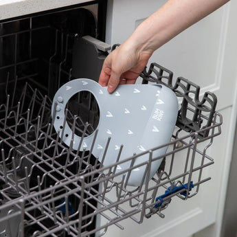 Placing a Bumkins Silicone Bib: Hearts with catch-all pocket into an open dishwasher rack.