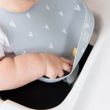 A baby in a Bumkins Silicone Bib: Hearts reaches into the food-safe pocket while sitting in a high chair.