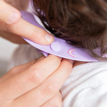 Adjusting a Bumkins Silicone Bib: Rainbows, ensuring baby safety during messy mealtime.