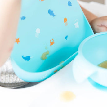 Baby in a Bumkins Silicone Bib: Ocean Life, enjoying mealtime from a matching bowl.