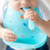 Close-up of a baby wearing a Bumkins Silicone Bib: Ocean Life, holding and chewing on a teething toy.