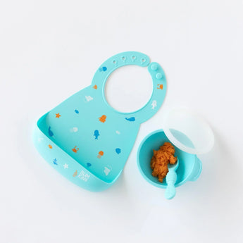 Silicone Bib: Ocean Life by Bumkins, shown with orange baby food and spoon—ideal for messy meal times with ocean-themed designs.