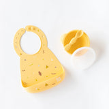 Bumkins Camp Gear: Yellow silicone baby bib with tiny drawings, matching bowl with lid, and spoon for handling any mealtime mess.