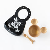 Black Bumkins Silicone Bib: Mickey + Minnie Mouse, gold bowl with ears, and spoon on white backdrop—ideal for little ones!.