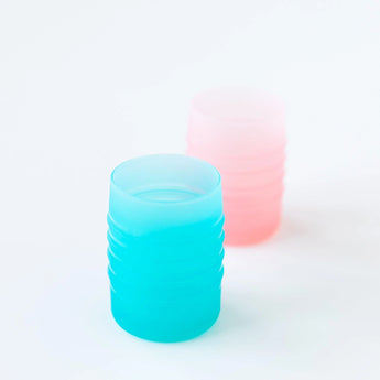 Two Bumkins Silicone Starter Cups: blue and pink. Translucent with ribbed designs, ideal for open cup drinking on a light background.