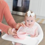 Smiling baby in high chair with white bow wears Bumkins Starter Bib. Easy-clean waterproof fabric. Kitchen in background.