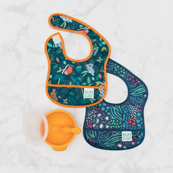 Two Bumkins Jungle & Animal Prints Starter Bibs with an orange silicone suction bowl on white marble. Safety tested for peace of mind.