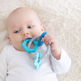 A baby lies in a white onesie with food-safe Silicone Teething Charms: Blue by Bumkins, aiding motor skills on a soft blanket.