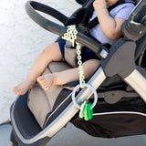 A baby in a stroller, wearing gray, enjoys a Bumkins Green Silicone Teething Charm, made from food-safe silicone for motor skill development.