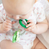 Baby in a floral onesie chewing on Bumkins Silicone Teething Charms: Green, made of food-safe silicone for motor skills development.