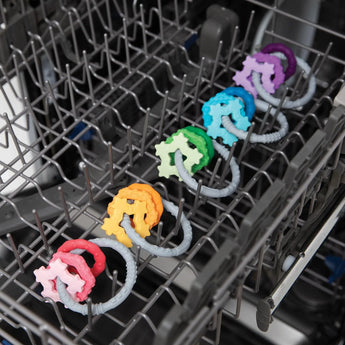 Bumkins Silicone Teething Charm in Green, showcasing its vibrant design and food-safe material, arranged in a dishwasher rack.