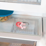 Close-up of an open fridge shelf with a pastel-colored Bumkins Silicone Teething Charms: Pink beside a covered bowl of food.