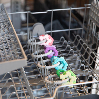 Bumkins Silicone Teething Charms: Blue are neatly arranged in rows inside an open dishwasher.