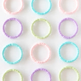 Four Bumkins Silicone Teething Rings in pastel shades, made of food-safe silicone, arranged to soothe sore gums.