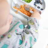 A baby in a Bumkins Sleeved Bib: Cacti reaches for food on a tray with carrots, blueberries, and green puree.