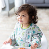 Toddler in a Bumkins Sleeved Bib: Cacti, sitting in a high chair with fork in hand, ready to enjoy dinner.