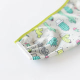 Close-up of Bumkins Sleeved Bib: Cacti, featuring a colorful cactus print and green edge, made with waterproof fabric for an adjustable fit.