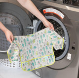 A person puts a Bumkins Sleeved Bib: Cacti into a front-loading washing machine.