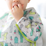 Child wearing Bumkins Sleeved Bib: Cacti, fingers in mouth; adjustable fit ensures comfort, set against a plain white background.