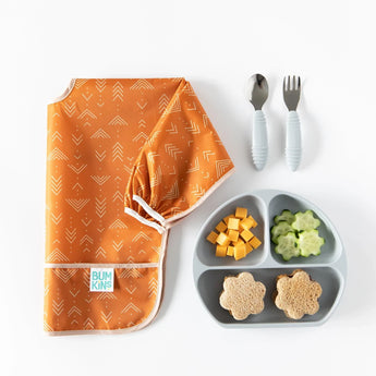 Bumkins Grounded sleeved bib with a gray plate featuring cheese cubes, cucumbers, sandwich flowers, spoon & fork.