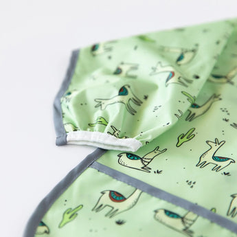 Close-up of Bumkins Sleeved Bib: Llamas, waterproof with llama and cacti print and gray trim, angled for effortless cleaning.