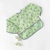 Bumkins Sleeved Bib: Llamas features waterproof fabric and pocket; shown with baby fork and spoon on white background.