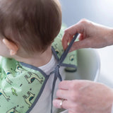 A person ties a Bumkins Sleeved Bib featuring llamas around a babys neck, made from waterproof fabric for easy cleaning.