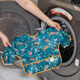 A Bumkins Sleeved Bib: Jungle with colorful animal prints and waterproof fabric is placed in the washing machine for laundry.