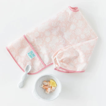 The Sleeved Bib: Lace by Bumkins in light pink floral, with a white spoon and shrimp-and-lemon bowl is ideal for baby-led weaning.