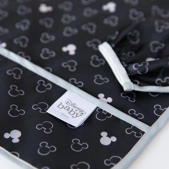 Close-up of a black and white Disney-themed Bumkins Sleeved Bib with Mickey Mouse patterns, featuring a stain and odor resistant label.