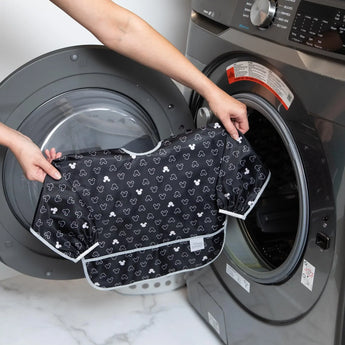 Someone loading a Bumkins Sleeved Bib with Mickey Mouse Icon in Black + White into the washing machine.